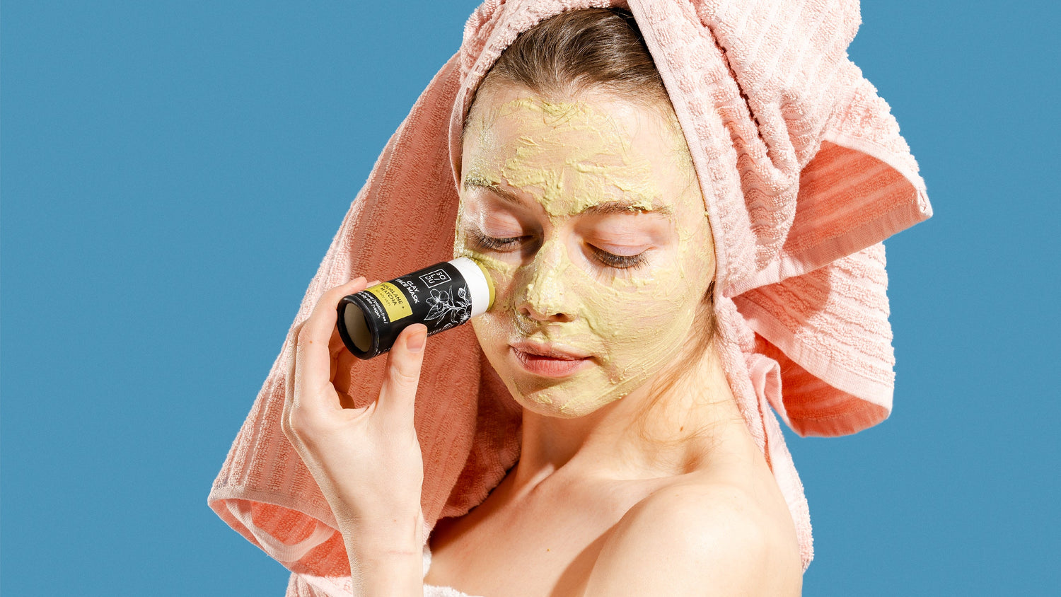 Woman applying a facial mask with a bottle of product against a blue background